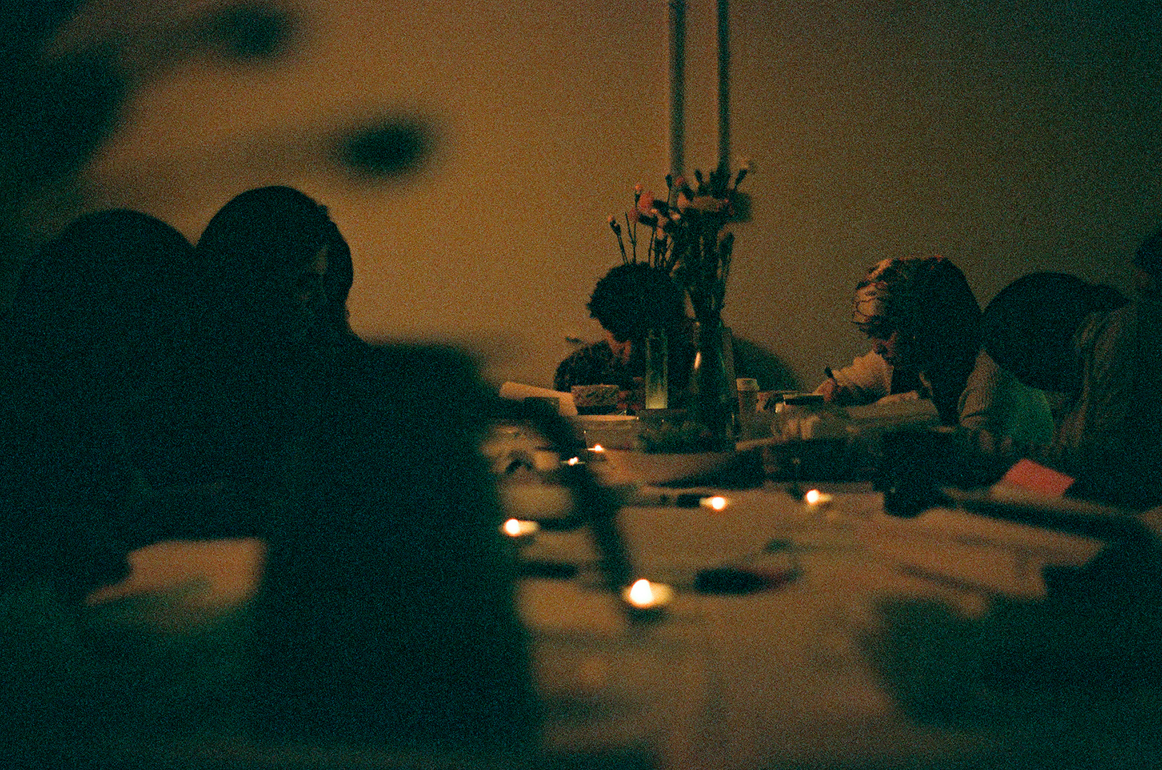 Photo with very low lighting that depicts different females writing or drawing at a table with candles on it.